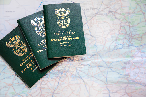 Three South African passports agains a  out of focus map of South Africa. Concept for covid travel restrictions and travel ban