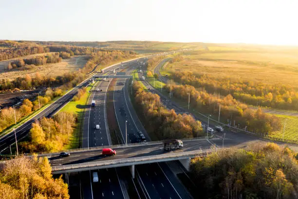 Aerial view of a UK Motorway and overpass bridge through picturesque countryside at sunset