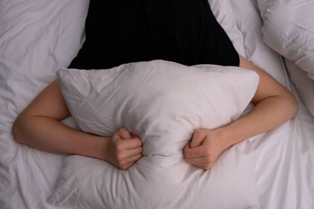 istock man lying in bed and covers his head with a pillow. Fights insomnia, noise or getting up early in the morning. 1355836646