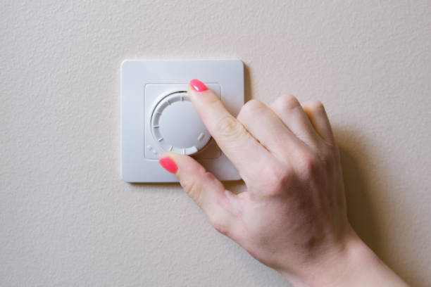 Woman's hand adjusts the lighting with a dimmer lever. An electronic device designed to change electrical power Woman's hand adjusts the lighting with a dimmer lever. An electronic device designed to change electrical power. Used to adjust the brightness of the light emitted by incandescent lamps or LEDs. dimmer switch photos stock pictures, royalty-free photos & images
