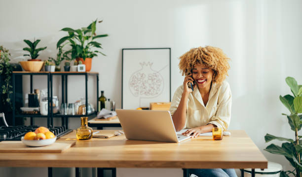 istock Beautiful Cheerful Woman Having a Phone Call while Working on a Laptop 1355840235