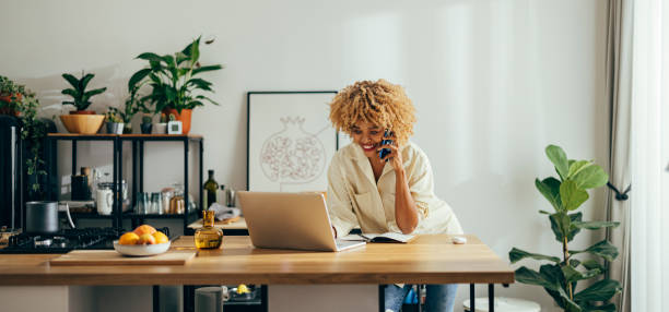 Beautiful Cheerful Woman Having a Phone Call while Working on a Laptop