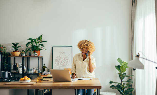 istock Beautiful Cheerful Woman Having a Phone Call while Working on a Laptop 1355840246