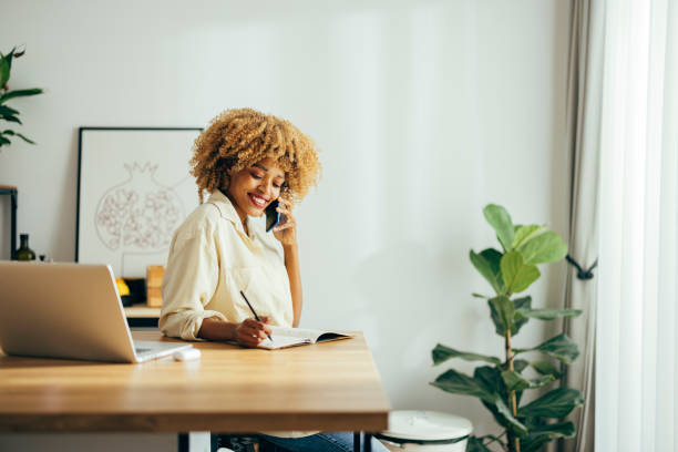 istock Beautiful Cheerful Woman Having a Phone Call while Working on a Laptop 1355840254