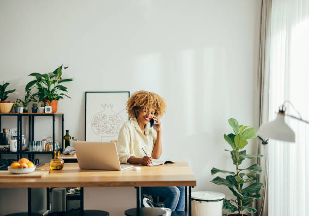 istock Beautiful Cheerful Woman Having a Phone Call while Working on a Laptop 1355840255