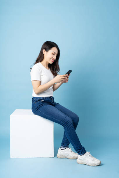 istock Asian girl portrait sitting on white cube, isolated on blue background 1355843877