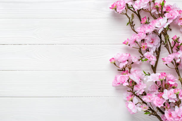 istock Sakura branches on a wood table. Pink cherry blossom on white wooden background. Frame border. Template with copy space. Pattern with place for text. Spring mockup. Greeting card, layout. 1355843972