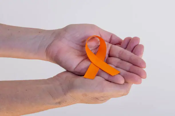 orange ribbon in hands. campaign to prevent skin cancer, melanoma, December orange