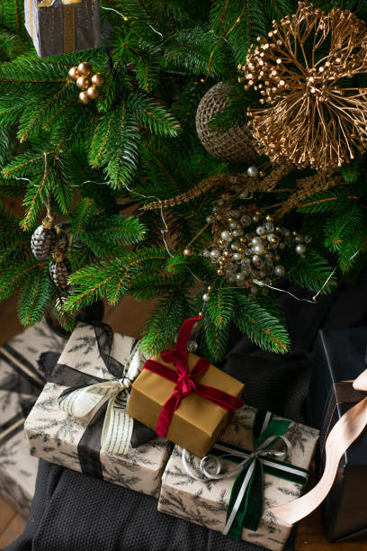 Luxury gift boxes under Christmas tree, New Year home decorations, wrapping of Santa presents, festive tree decorated with garland, baubles, traditional celebration. Vertical