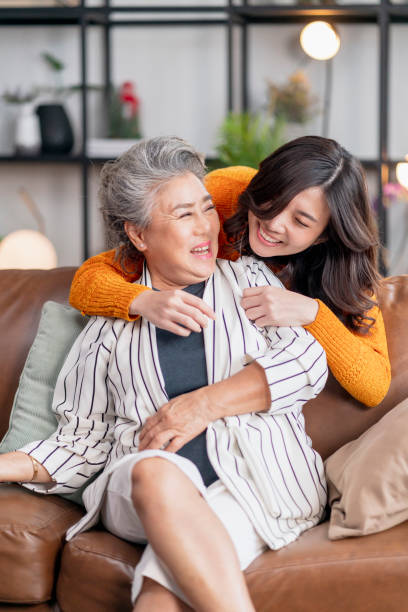 glück asiatische familie candid der tochter umarmen großeltern mutter senior ältere mutter gemütlich entspannen auf sofa couch im wohnzimmer, schöne familie von mutter und tochter zusammen, umarmen und küssen zu hause - people care surprise love stock-fotos und bilder