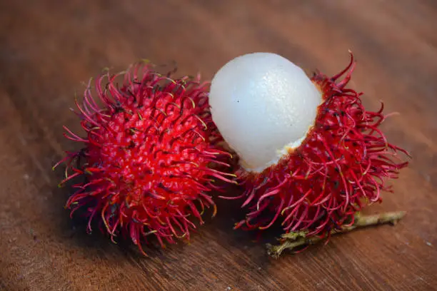 Photo of Red Rambutan fruit with inner flesh visible on wooden table