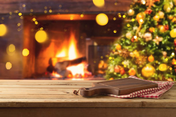 istock Empty wooden table with cutting board over Christmas tree and fireplace background.  Christmas and New Year mock up for design and product display. 1355849098