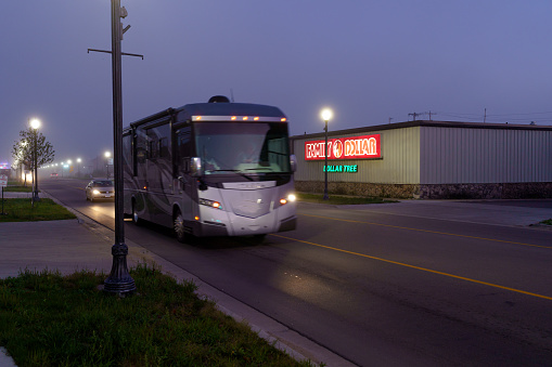 Munising, Michigan USA  - October 6, 2021 : A large RV Motorhome passes the Family Dollar Store in Munising Michigan.  Shot at dusk the sign is lit and next to the main road.