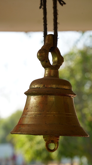 Bronze bell in indian temple in the green crops blur background. Hindu temple brass bell hanging in gold color.