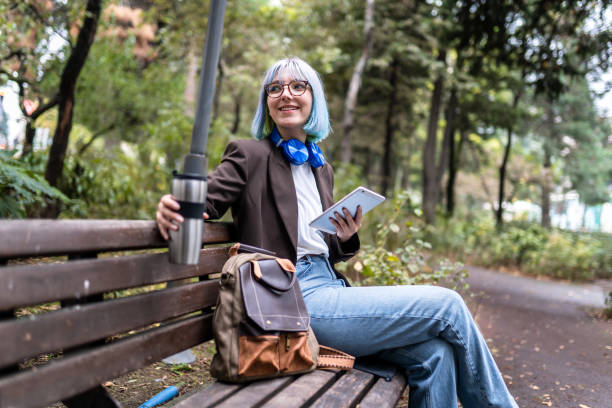 Young woman sitting in public park after work and drinking coffee from thermos stock photo
