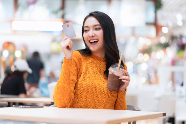 happiness smart casual asian female customer sit exited hand hold credit card mockup and  cold drink cashless money technology trend new kifestyle,asian female smile use credit card in food court stock photo