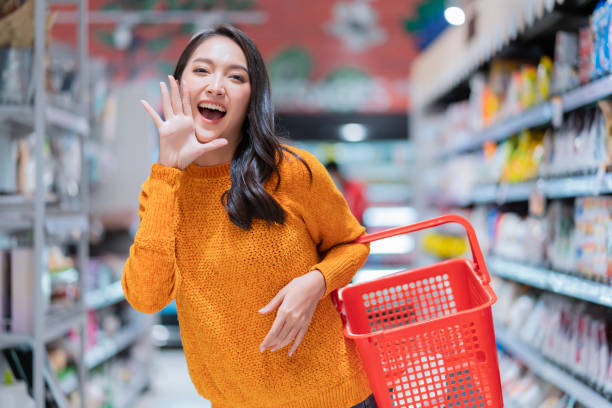 felicidade alegre saiu mulher asiática casual mão de pano de tecido segurar vazio gesto de mão cesta de compras anunciar boas notícias ou nova promoção para câmera, mulher asiática sorrindo em supermercado mercearia - convenience store merchandise consumerism customer - fotografias e filmes do acervo