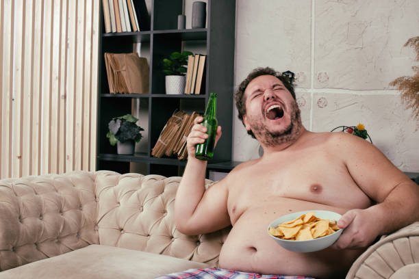 istock Funny fat man drinking beer at home. 1355857881
