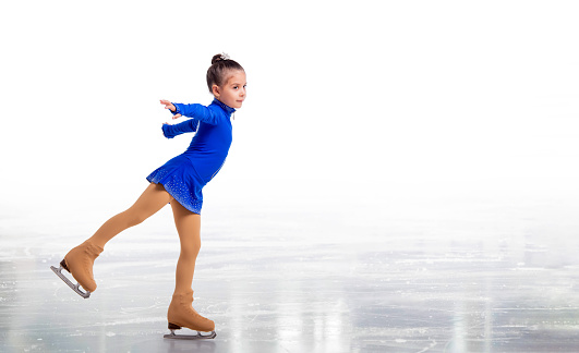 Little young figure skater posing in blue training dress on ice on white background