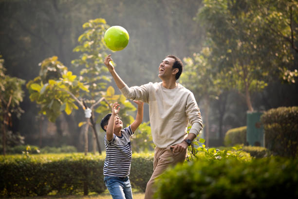 padre e hijo divirtiéndose mientras juegan con la pelota en el parque - park child asia lifestyles fotografías e imágenes de stock