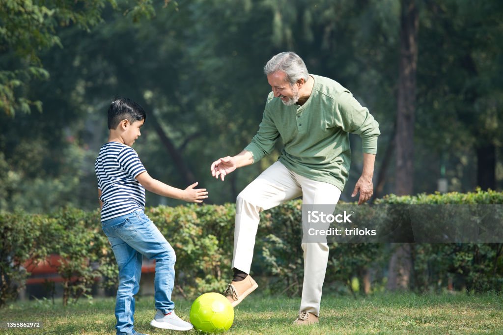 Senior man playing with grandson at park Senior man and grandson playing with ball at park Playful Stock Photo