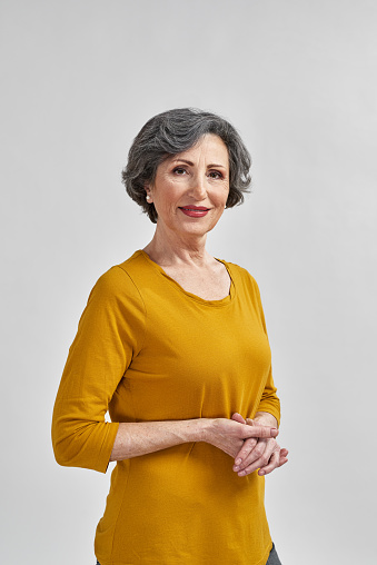 Portrait of a mature woman wearing a green shirt laughing while standing in front of a light gray background