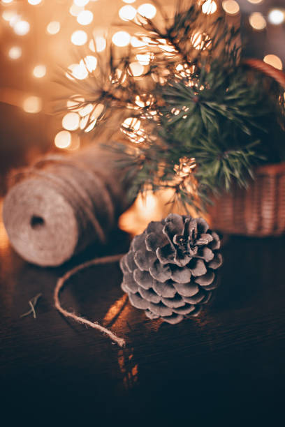 A pine cone lies on a wooden base against a background of green pine branches in a basket, jute twine and Christmas lights, front view.