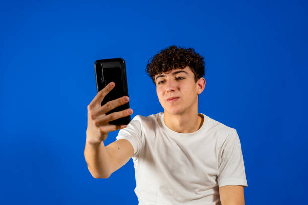 istock Smiling young man guy 20s in white shirt isolated on pastel blue wall background studio portrait. People lifestyle concept. Mock up copy space. Using mobile phone, typing sms message 1355868853
