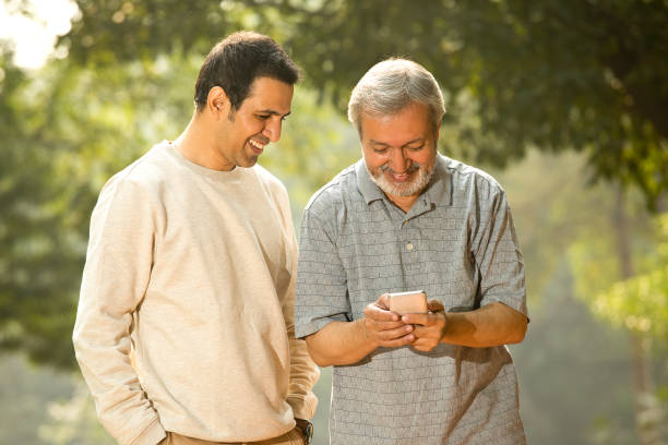 istock Senior man and son enjoying while using mobile phone at park 1355869096
