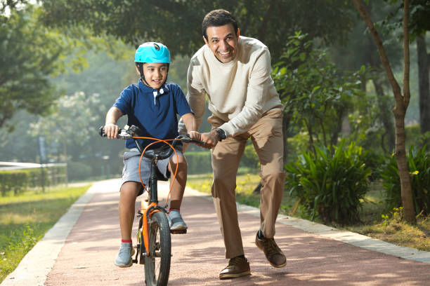 Boy learning bicycle with assistance of father at park stock photo
