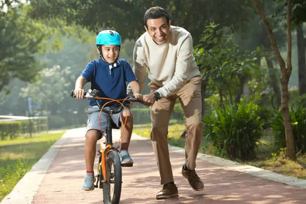 Photo of Boy learning bicycle with assistance of father at park