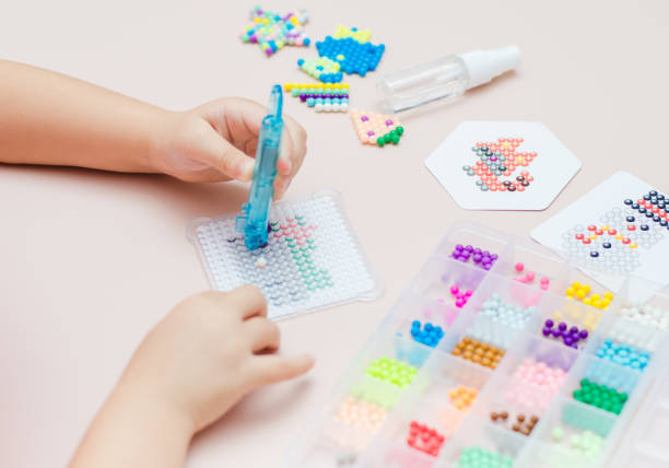 istock Children's educational game aqua mosaic, a small child inserts multicolored beads into the pattern with a special pen. 1355878742