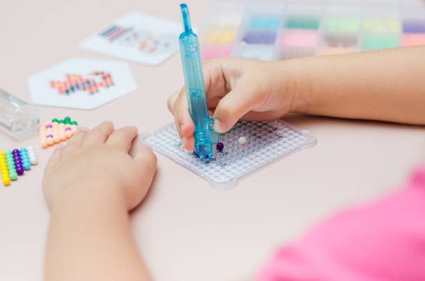 istock Children's educational game aqua mosaic, a small child inserts multicolored beads into the pattern with a special pen. 1355878744