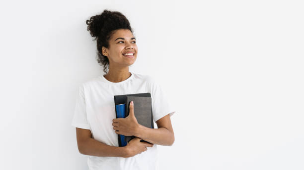 istock Young student girl looking aside, holding books in hands 1355887504