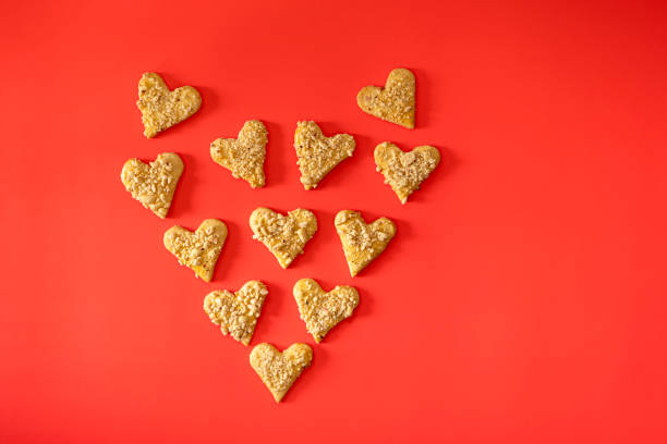 Shortbread cookies sprinkled with crushed peanuts in the shape of a heart on a red background, top view. Homemade cakes for breakfast. Copying a space.The concept of home-made food. Valentines Day.