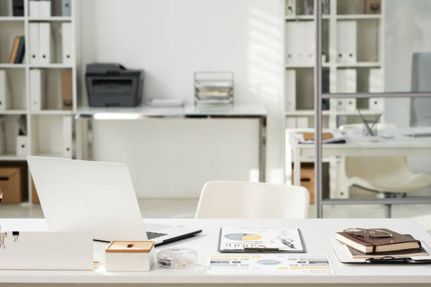istock Office interior with white table with open laptop, financial documents and organizer and chair 1355893091