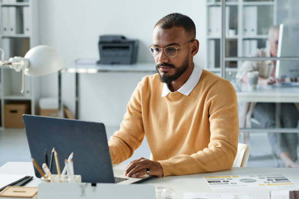 istock Concentrated young Biracial manager with beard sitting at office table and analyzing online file on laptop 1355894076