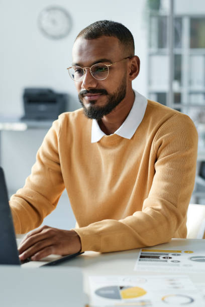istock Content young mixed race statistics expert with beard sitting at desk with documents and using laptop in office 1355894100