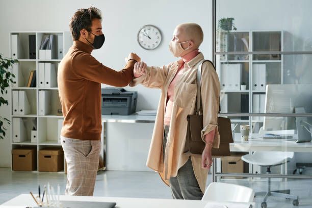 istock Young interracial colleagues in masks touching elbows while greeting each other in modern office 1355894951