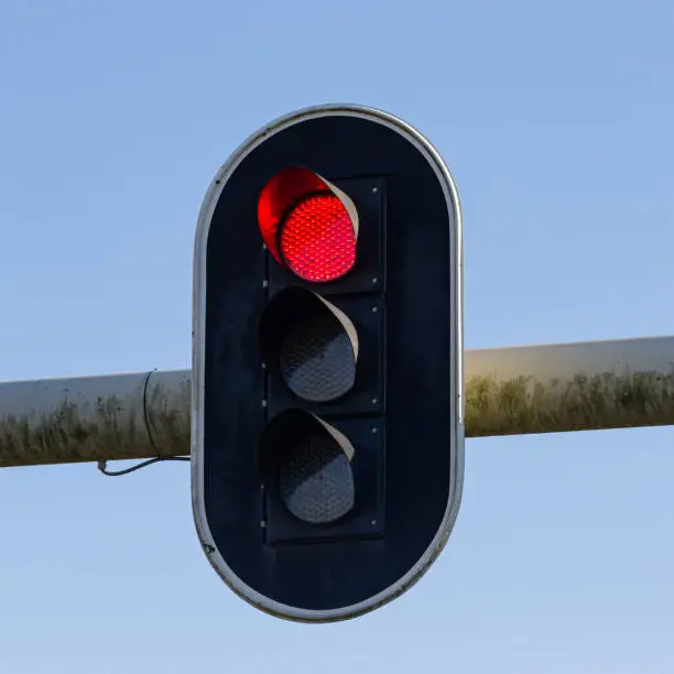 Daytime close-up of a single, weathered red light stoplight against a clear sky