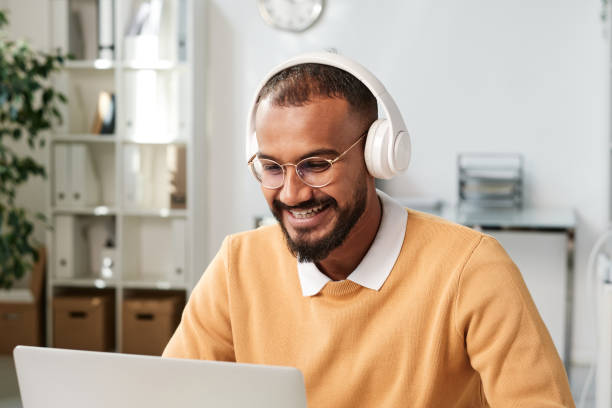 istock Cheerful young middle eastern manager in wireless headphones laughing while videoconferencing with business partner through laptop app 1355898787