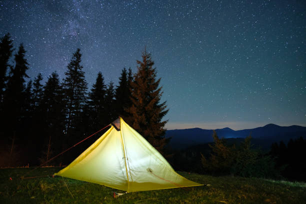 istock Brightly illuminated camping tent glowing on campsite in dark mountains under night stars covered sky. Active lifestyle and traveling concept. 1355900009