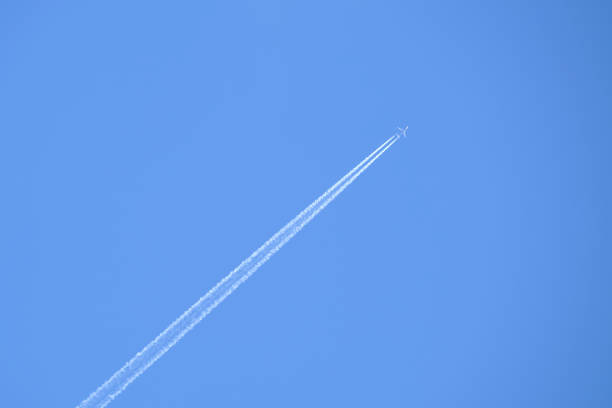 istock Distant passenger jet plane flying on high altitude on clear blue sky leaving white smoke trace of contrail behind. Air transportation concept. 1355900027