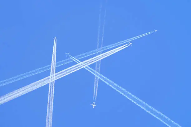Many distant passenger jet planes flying on high altitude on clear blue sky leaving white smoke trace of contrail behind. Busy air transportation concept.