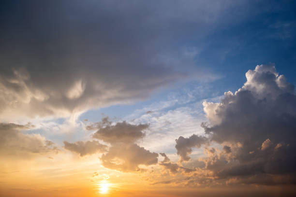 istock Dramatic yellow sunset landscape with puffy clouds lit by orange setting sun and blue sky. 1355900066