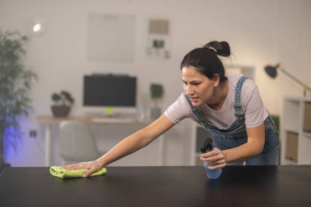 istock Woman cleaning table at home with spray bottle and rag 1355905617
