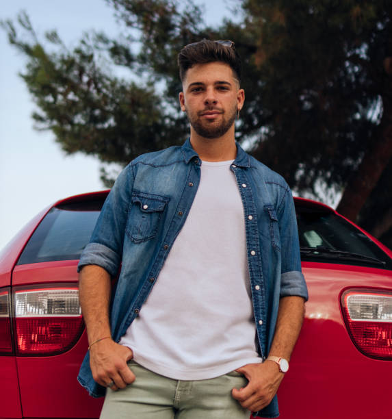 istock Handsome guy leaning on the back of a red car with neutral expression 1355906724