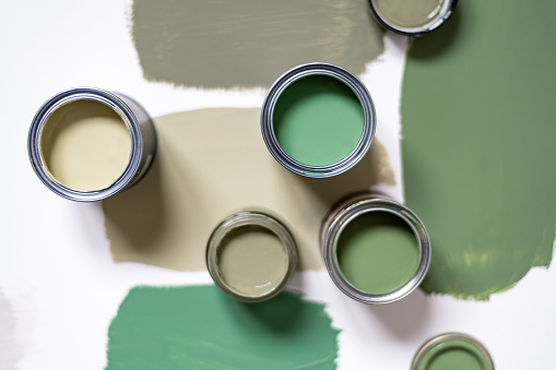 Tiny sample paint cans during house renovation, process of choosing paint for the walls, different green colors, color charts on background