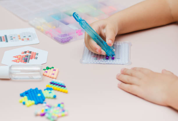 istock Children's educational game aqua mosaic, a small child inserts multicolored beads into the pattern with a special pen. 1355910483