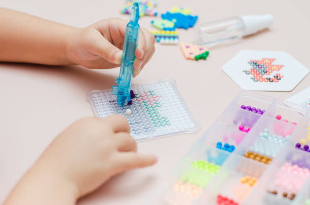 istock Children's educational game aqua mosaic, a small child inserts multicolored beads into the pattern with a special pen. 1355910484